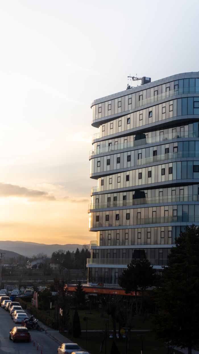 A modern glass building at sunset with a scenic view of cars and nature, offering urban aesthetics.