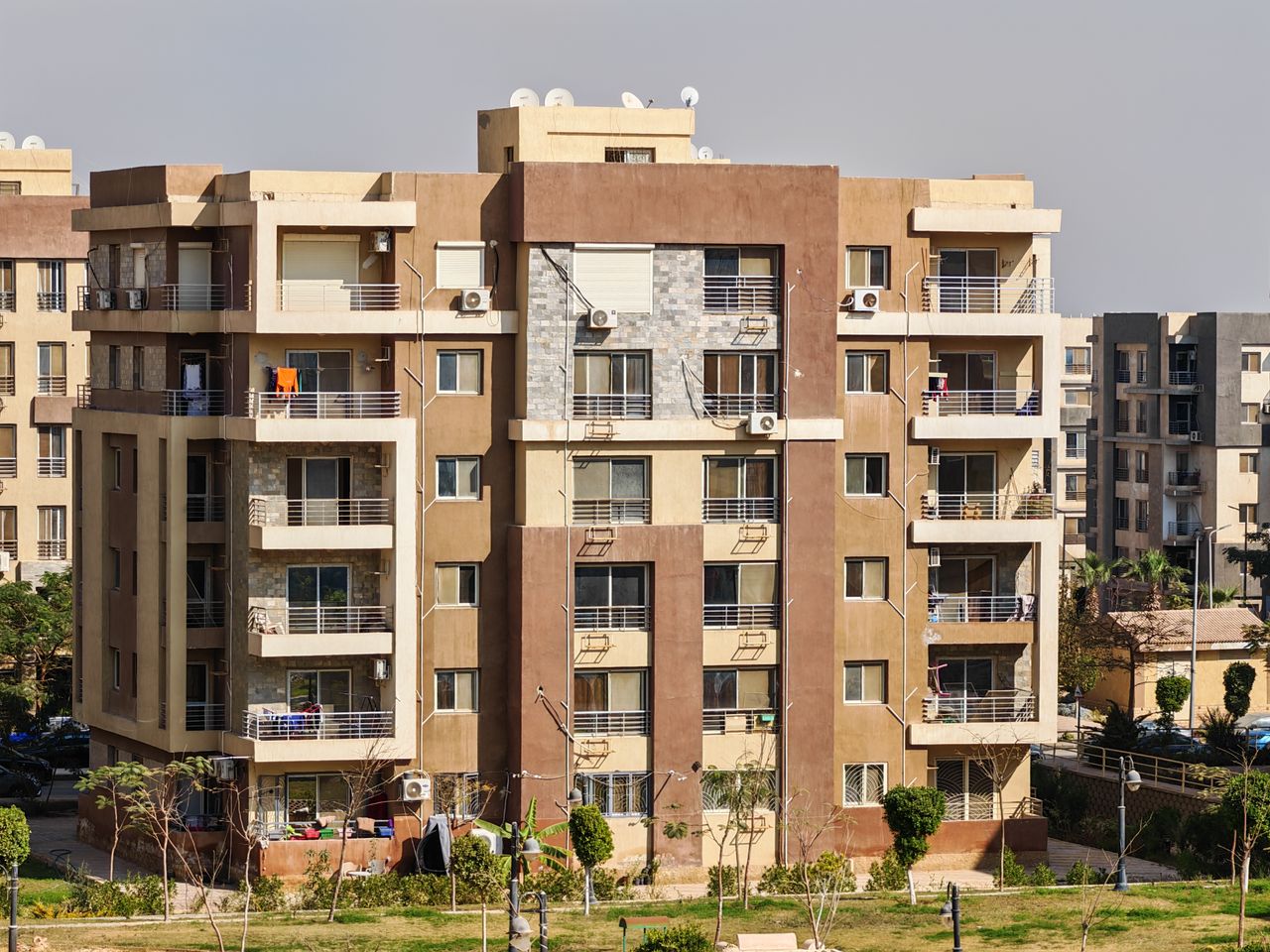A sunny urban scene of a modern apartment building exterior with balconies and greenery.
